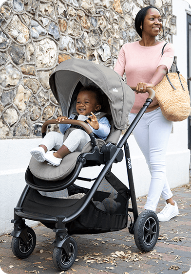 Lachende moeder duwt haar baby in een grijze versatrax. 