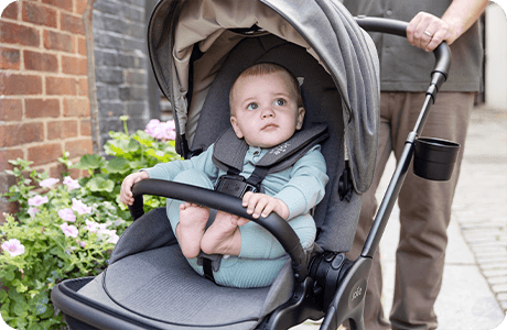 Lächelndes Kleinkind in einem Joie finiti Signature Kinderwagen in Hellgrau.